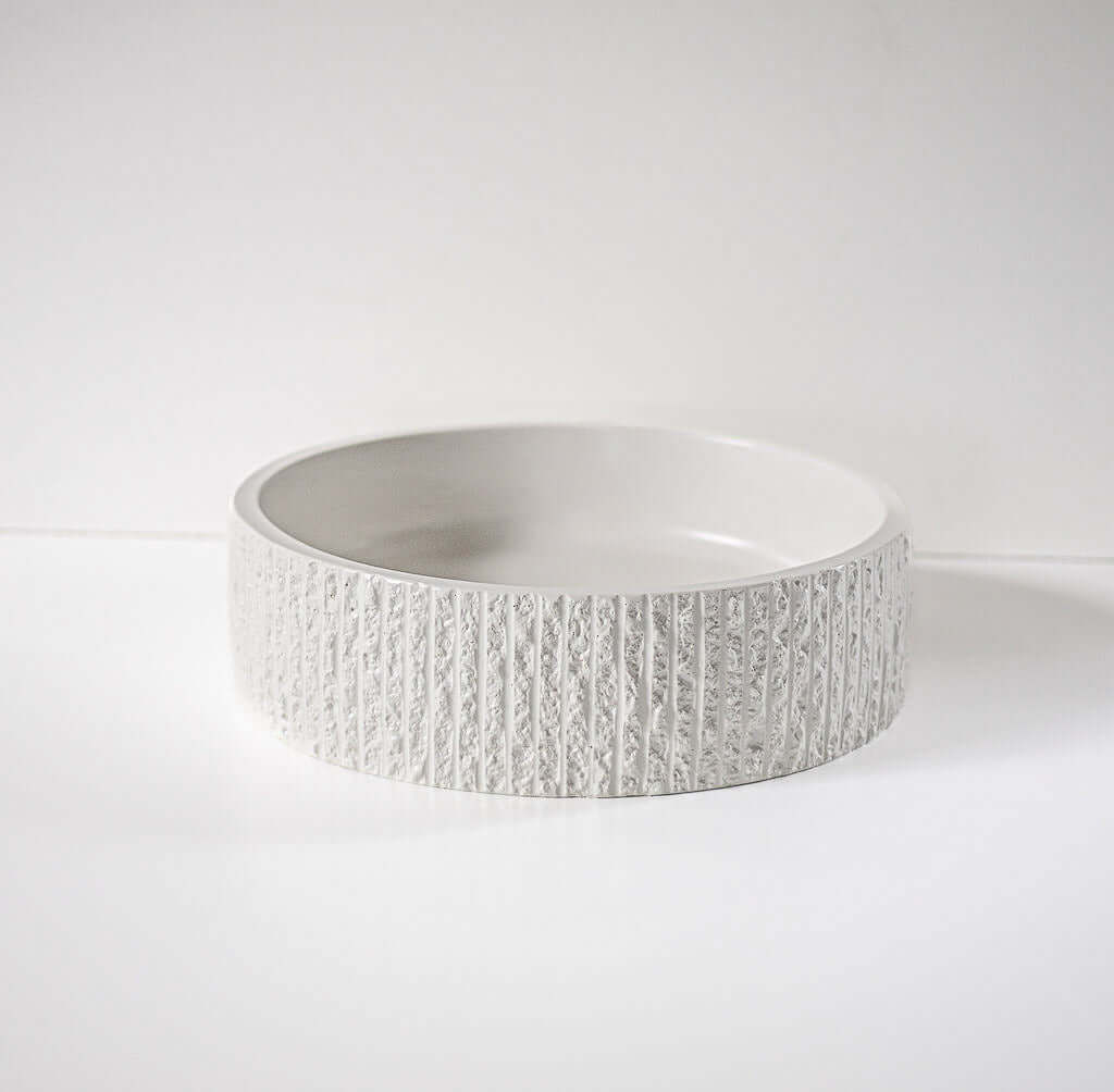 A textured, round ceramic bowl rests on a plain white surface, with its detailed exterior pattern highlighting a minimalist and modern design.