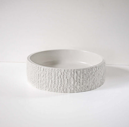 A textured, round ceramic bowl rests on a plain white surface, with its detailed exterior pattern highlighting a minimalist and modern design.