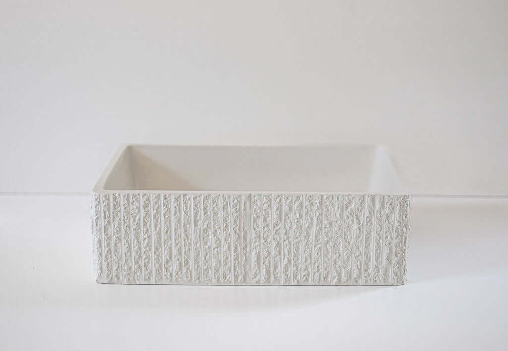 A rectangular, textured concrete container sits empty on a white surface, positioned against a light gray background.