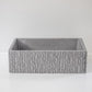 A rectangular, textured concrete planter with a ribbed surface rests on a smooth, white surface against a plain white background, creating a minimalist aesthetic.