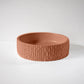 A textured, terracotta-colored round bowl rests on a smooth, white surface against a plain backdrop.