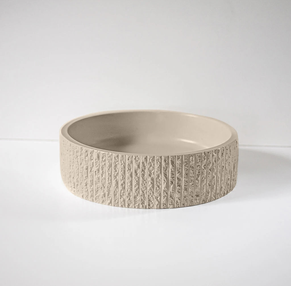 A beige round bowl with a textured, ridged exterior rests on a smooth, light-colored surface, set against a plain white background.