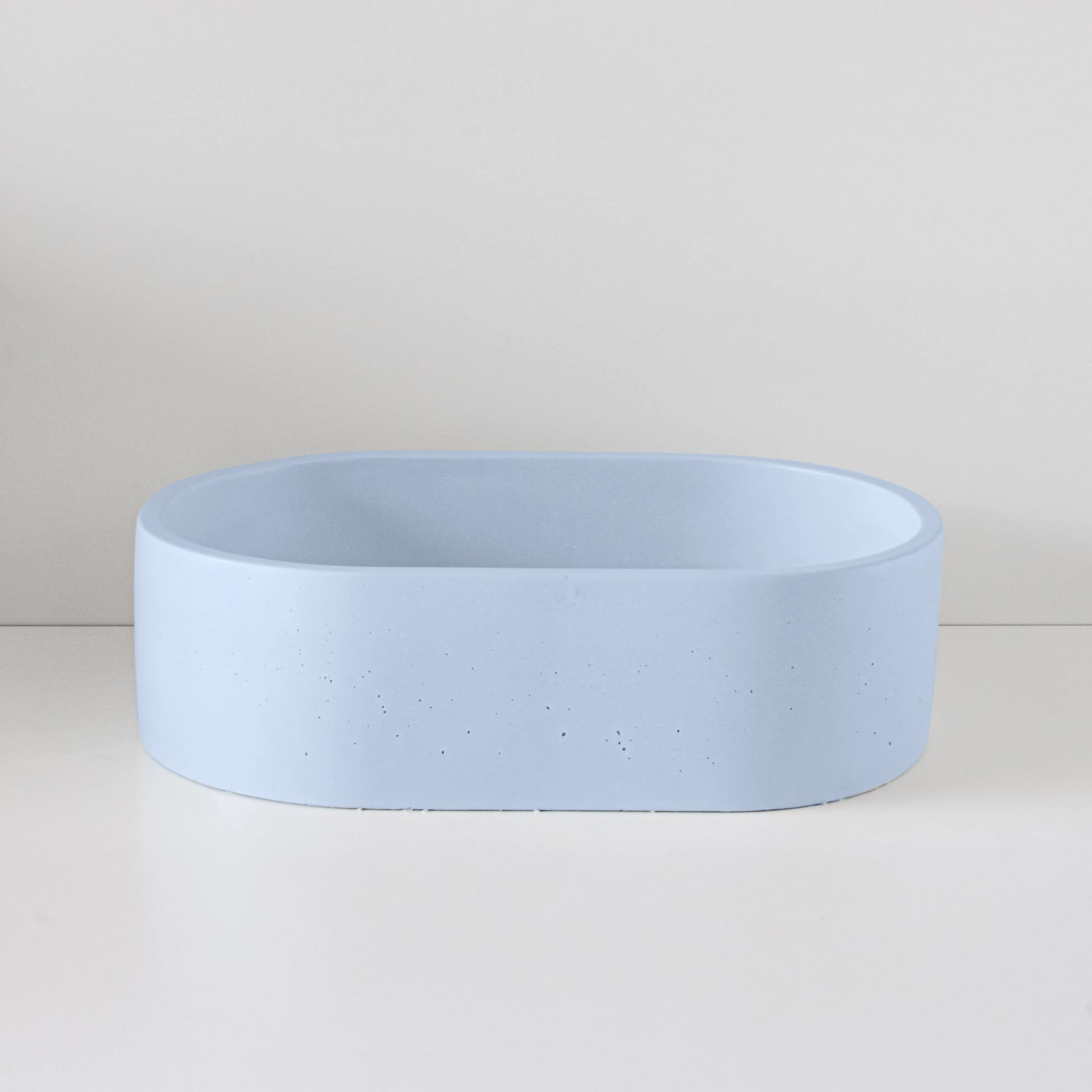 A light blue, oval-shaped cement basin sits unused on a white surface against a light gray background, emphasizing minimalist design and functionality.