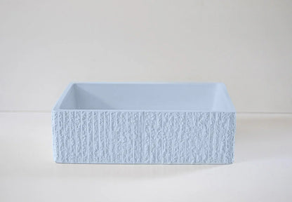 A rectangular, textured light blue box sits on a flat surface against a neutral background, displaying a simple and modern design.