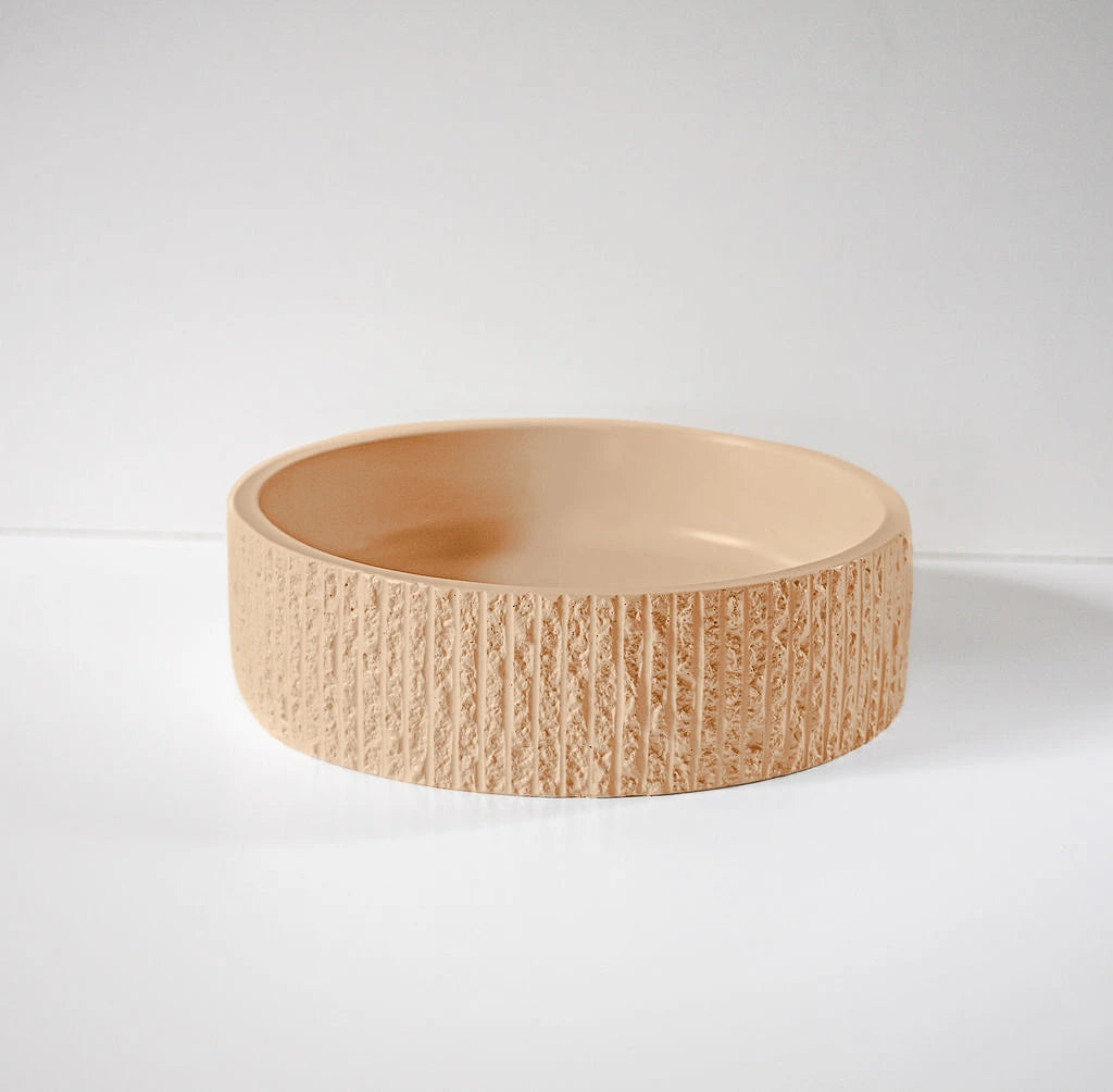 A textured, light brown bowl with a smooth interior rests upright on a plain white surface against a neutral backdrop, highlighting its modern, minimalistic design.