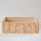 A rectangular, textured clay container sits empty on a smooth, light-colored surface against a plain background.