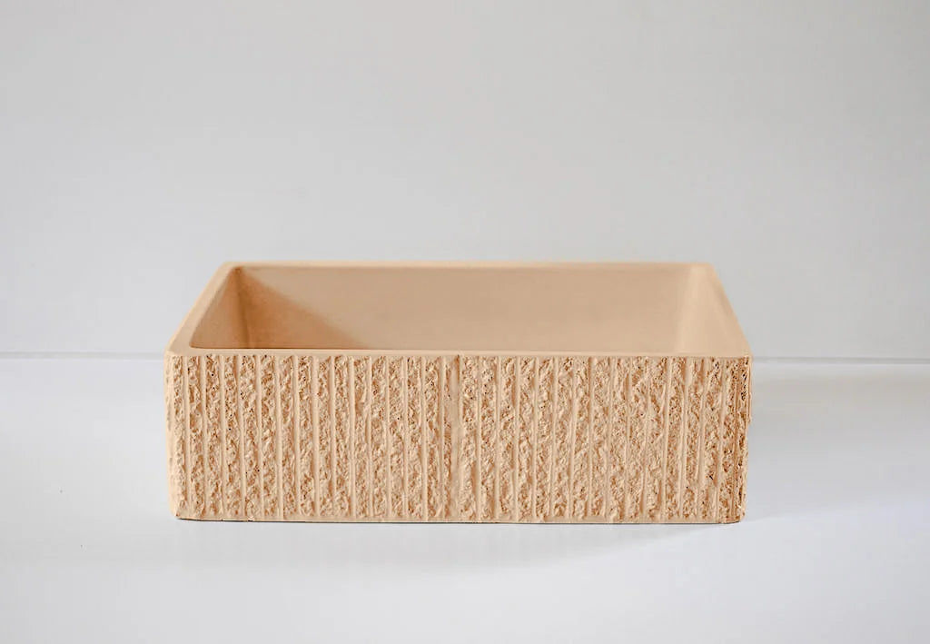 A rectangular, textured clay container sits empty on a smooth, light-colored surface against a plain background.