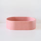 A pink, oval-shaped container sits on a white surface, suggesting modern simplicity and minimalist design within a clean, empty space.