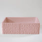 A rectangular, textured pink basin rests on a smooth, light-colored surface, with a minimalist backdrop, suggesting a modern design element.