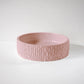 A textured pink ceramic bowl sits empty on a smooth, white surface, against a plain background.