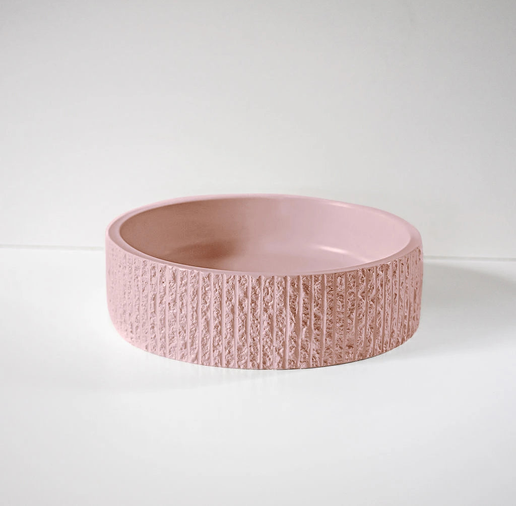 A textured pink ceramic bowl sits empty on a smooth, white surface, against a plain background.