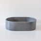 A smooth, gray oval concrete bowl sits on a white surface, with no additional objects or text present in the background.