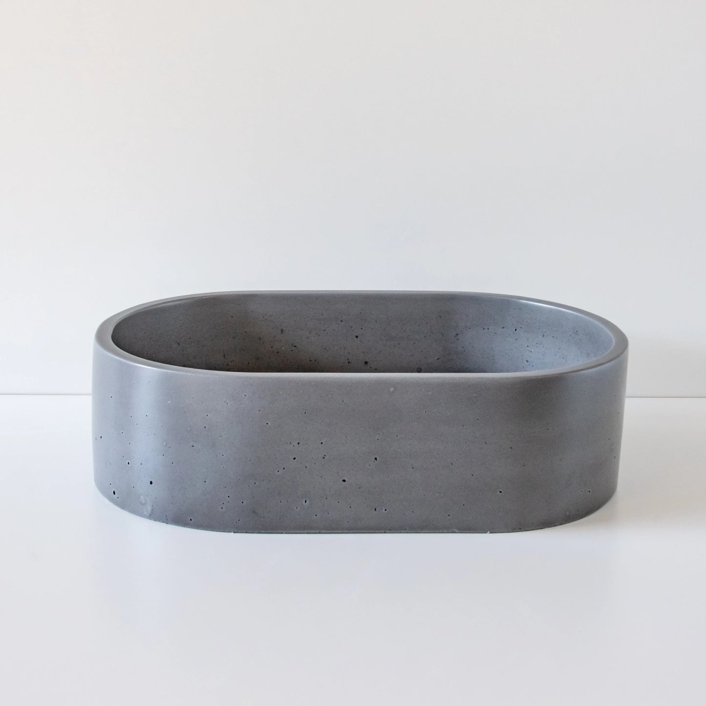 A smooth, gray oval concrete bowl sits on a white surface, with no additional objects or text present in the background.