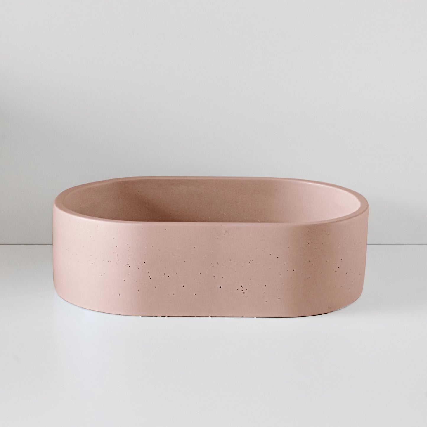 A pink, oval-shaped basin sits unused on a white surface, surrounded by a plain white wall.