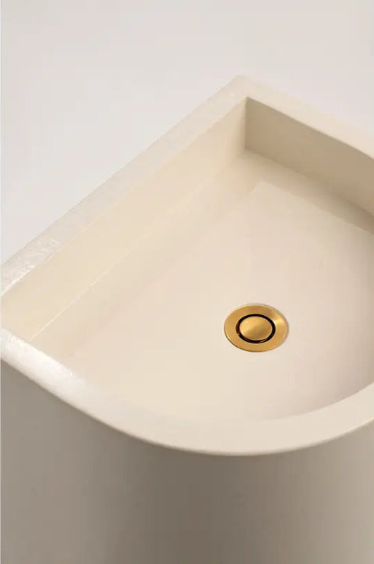 A close-up of the polished concrete half-moon pedestal basin's interior, highlighting the smooth finish and brass waste fitting.