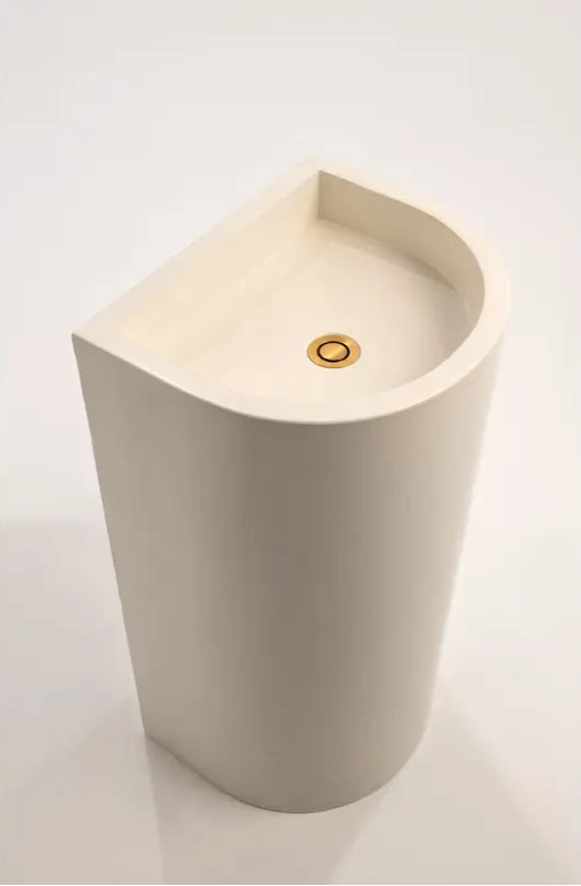 A top-down view of a polished concrete full-height half-moon pedestal basin with a rounded interior and a brass waste fitting.