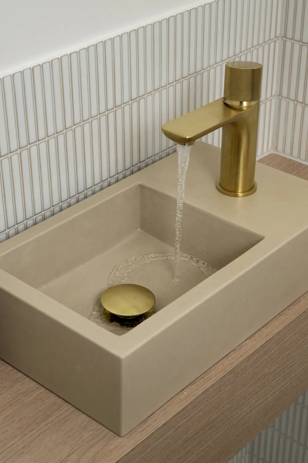 Concrete rectangular basin with brushed brass tap against white tiles