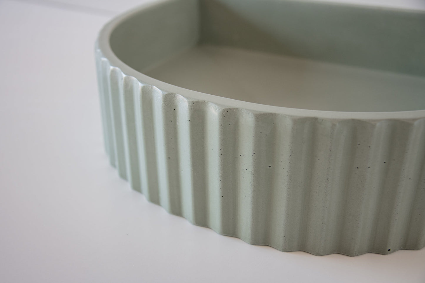 Curved, ribbed concrete bowl resting on a white surface, highlighting its textured detail and smooth interior.